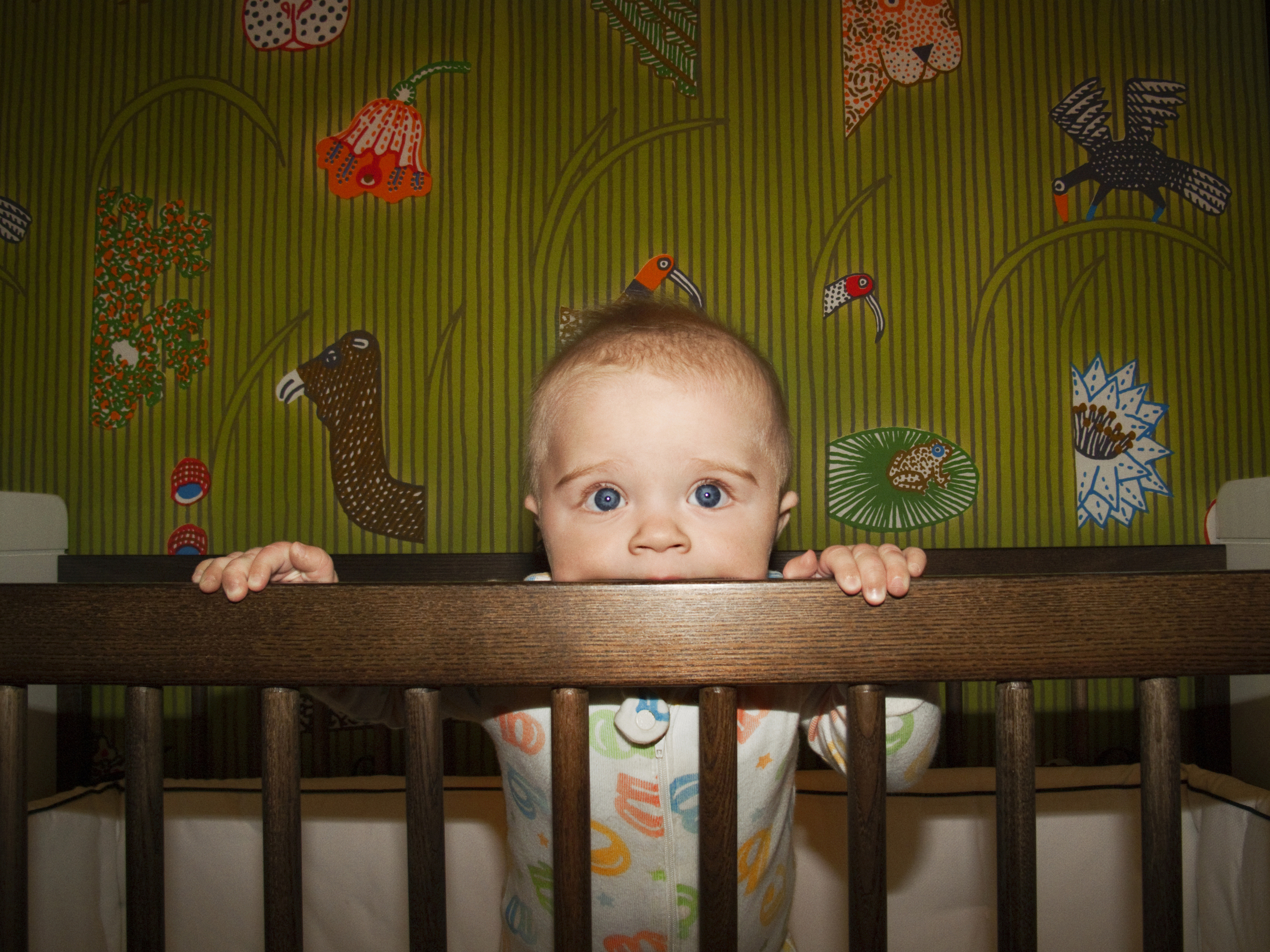 Baby standing in crib holding the rail at night