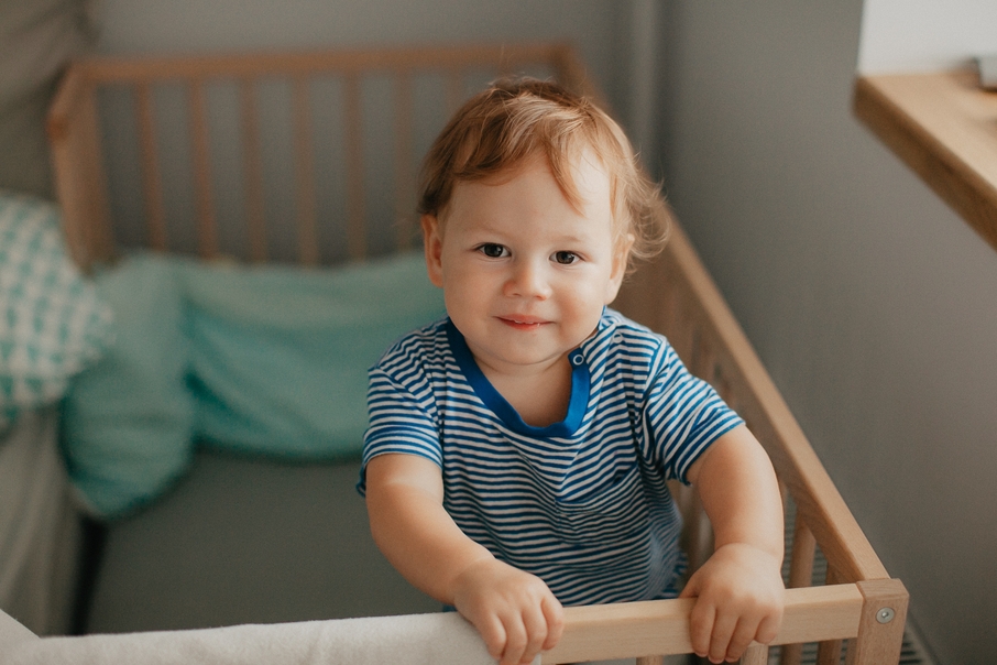 Toddler standing in a crib holding the rail at bedtime