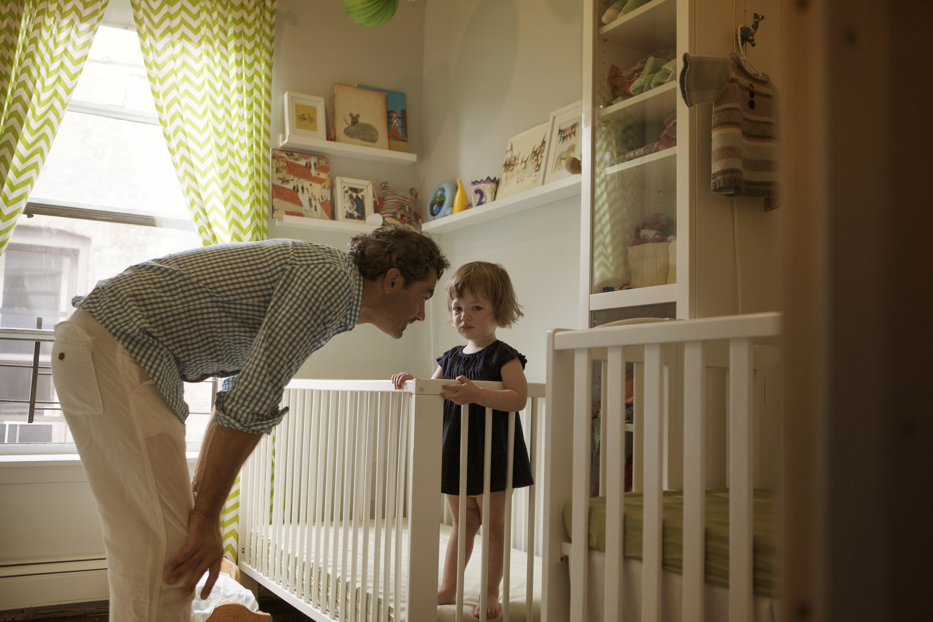 Toddler standing in crib as caregiver offers reassurance