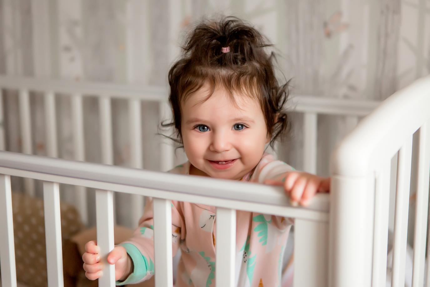 Toddler standing in a crib at bedtime looking wide awake