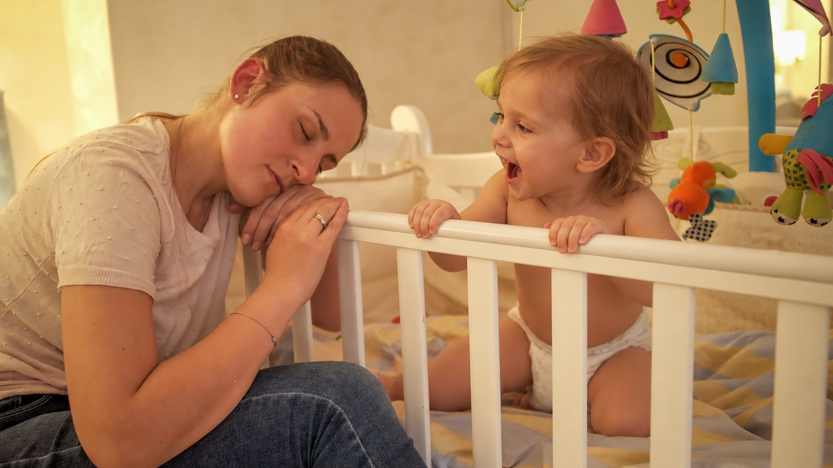 Parent sitting beside a toddler's crib at bedtime