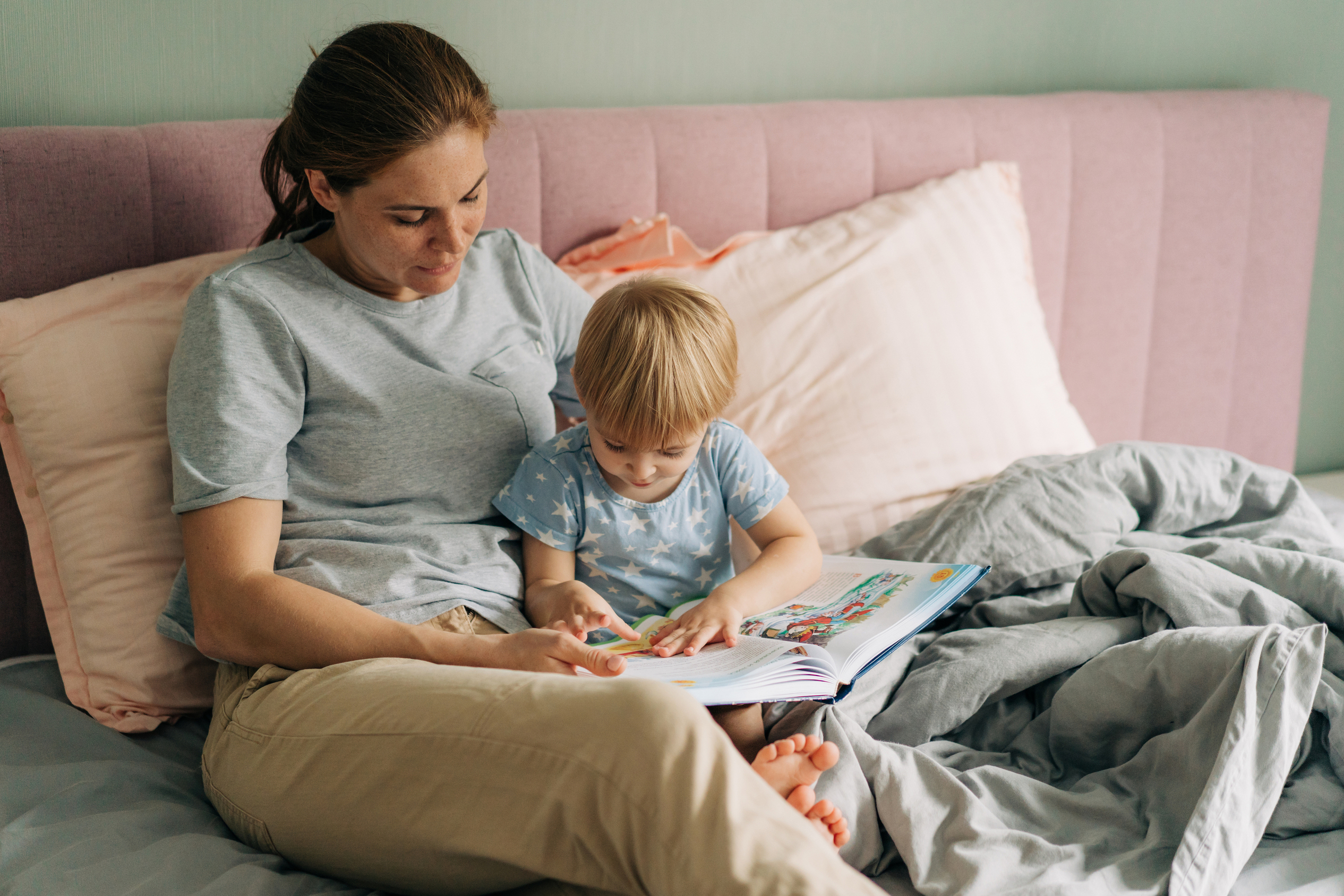 Parent reading a picture book to a toddler in a cozy bedroom