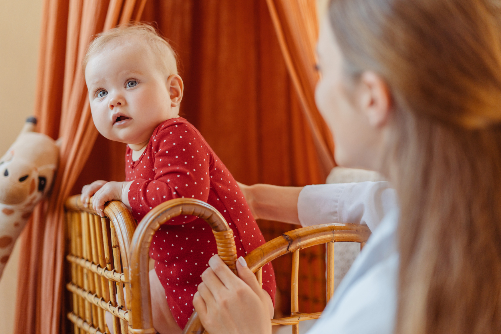 Baby practicing standing in a crib while parent watches