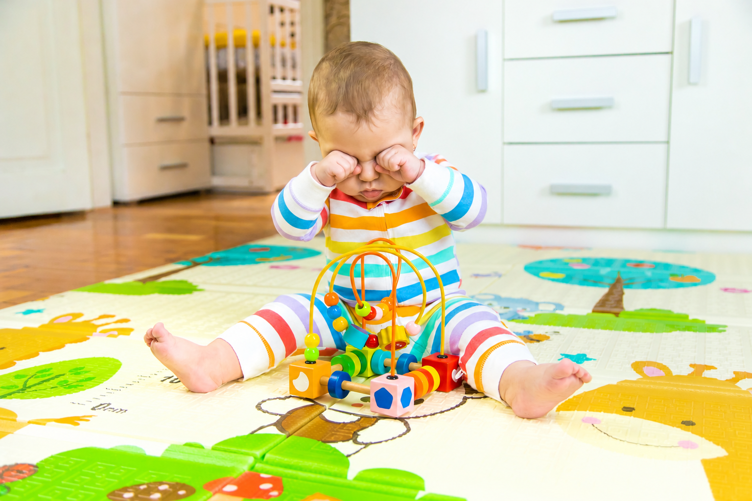 Tired baby rubbing eyes while sitting on a play mat