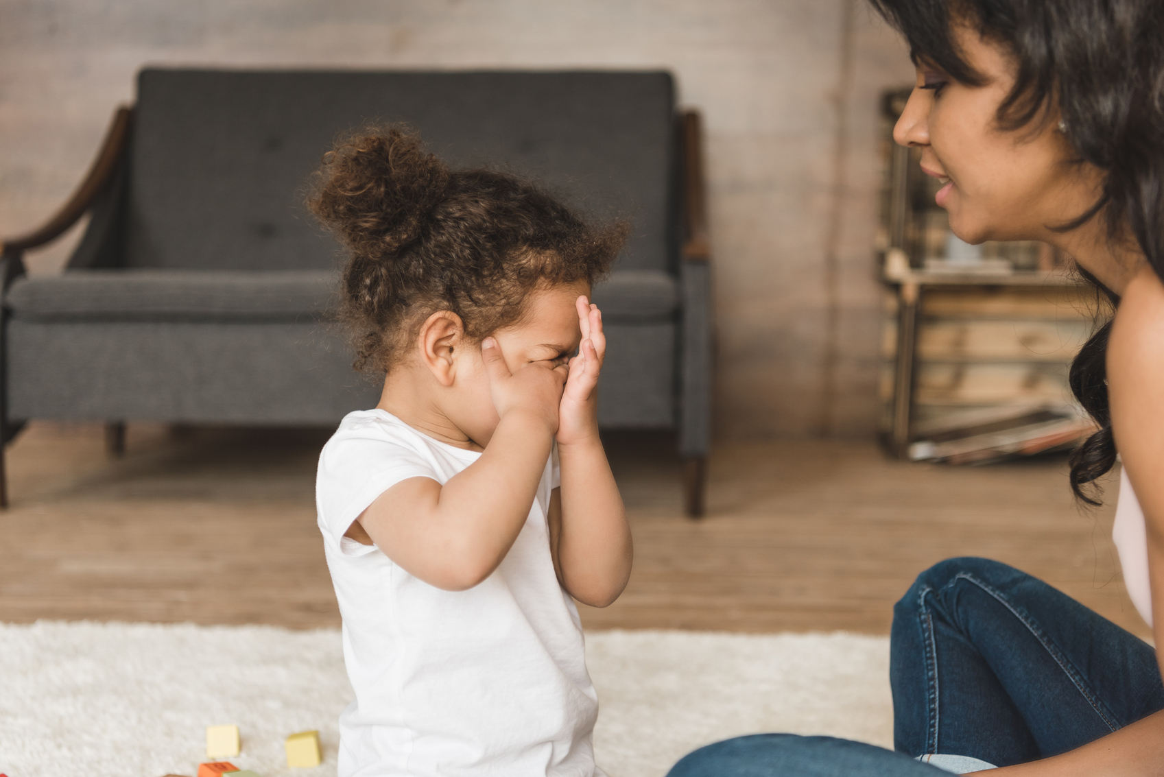 Tired toddler rubbing eyes while sitting on a rug with toys