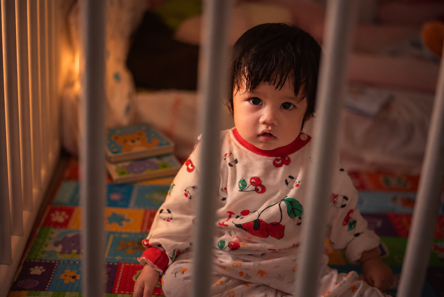 Toddler sitting awake in a crib at night with board books