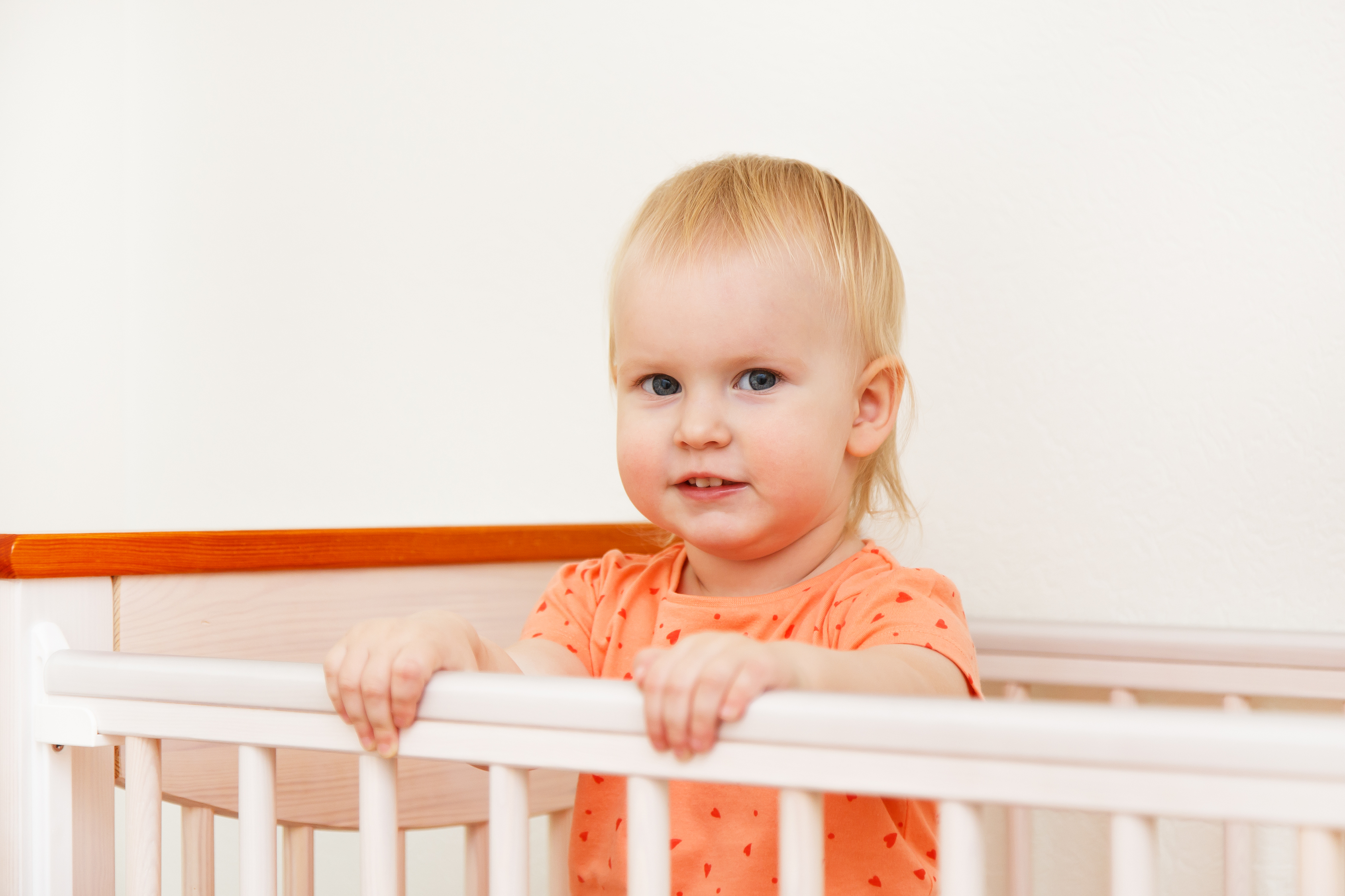 Toddler standing in crib holding the rail in a bright nursery