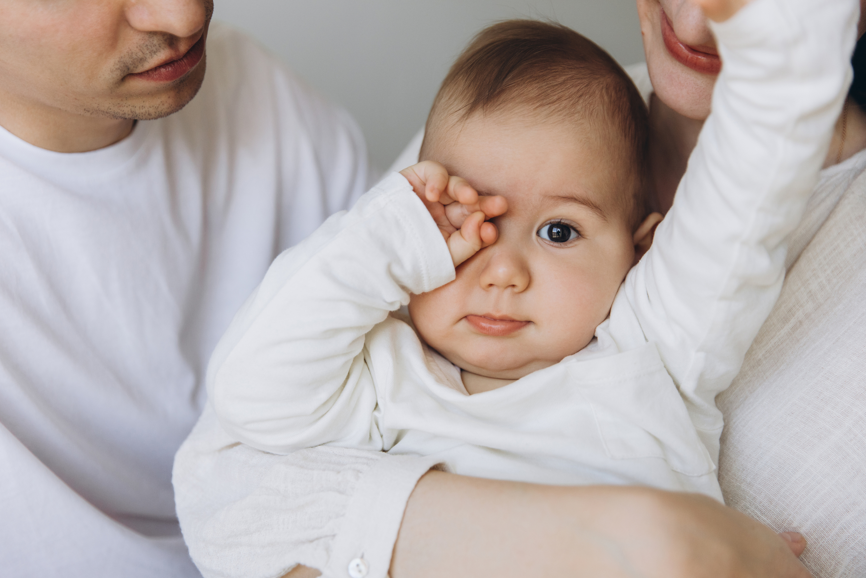 Overtired baby rubbing eyes in a parent's arms