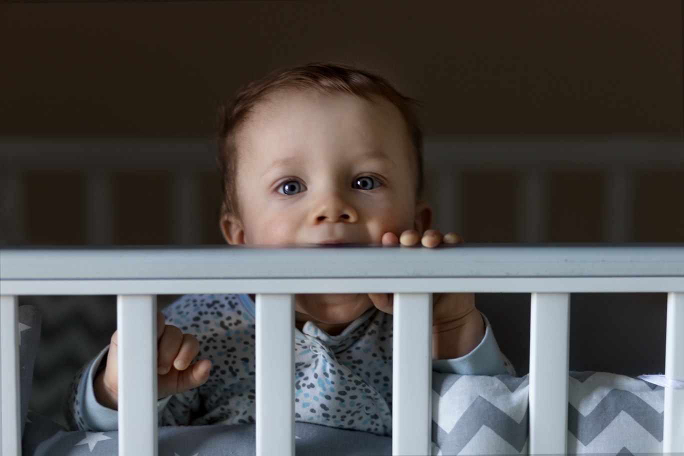 Toddler peeking over the side of a crib at night