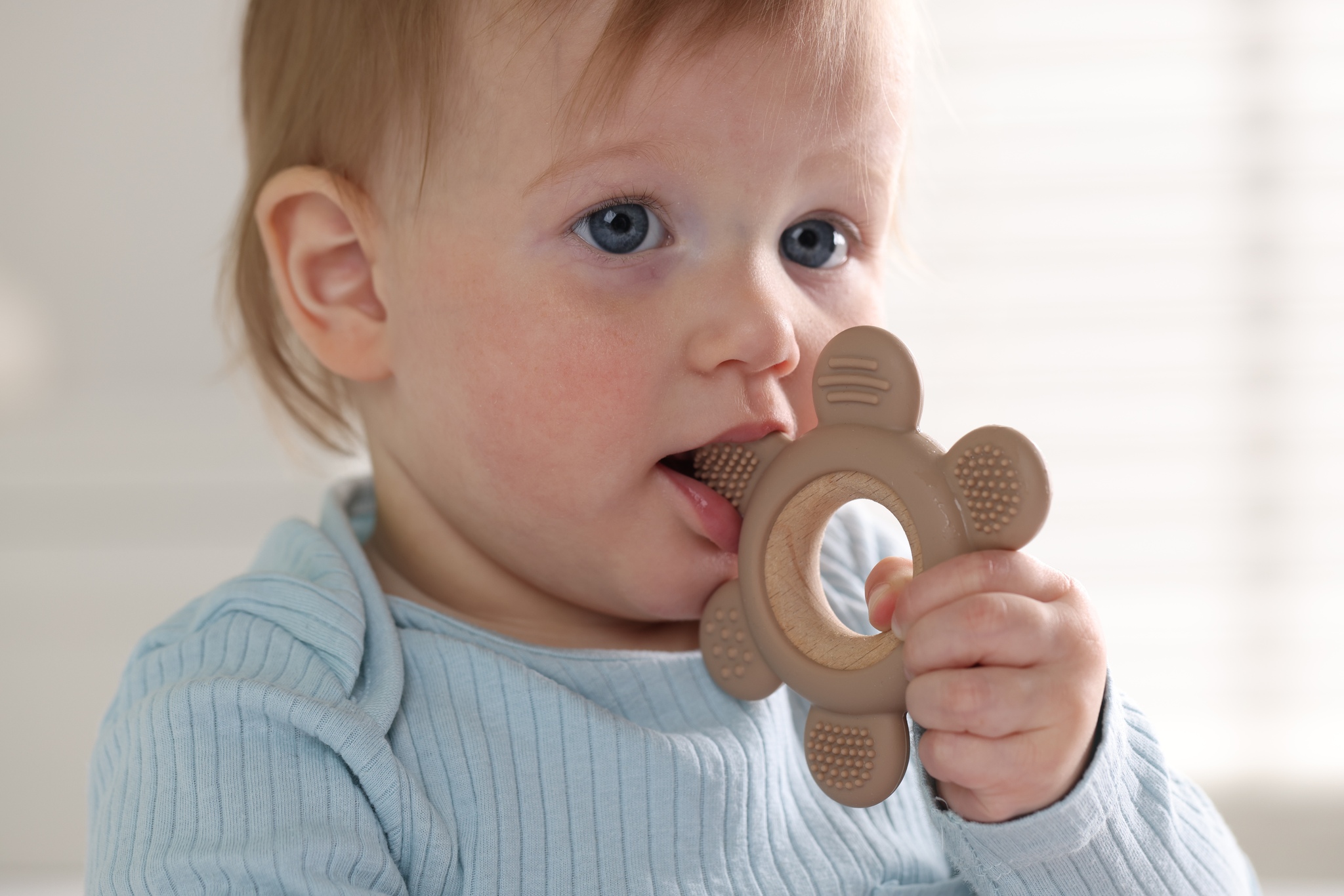 Toddler chewing on a teething ring at a small table